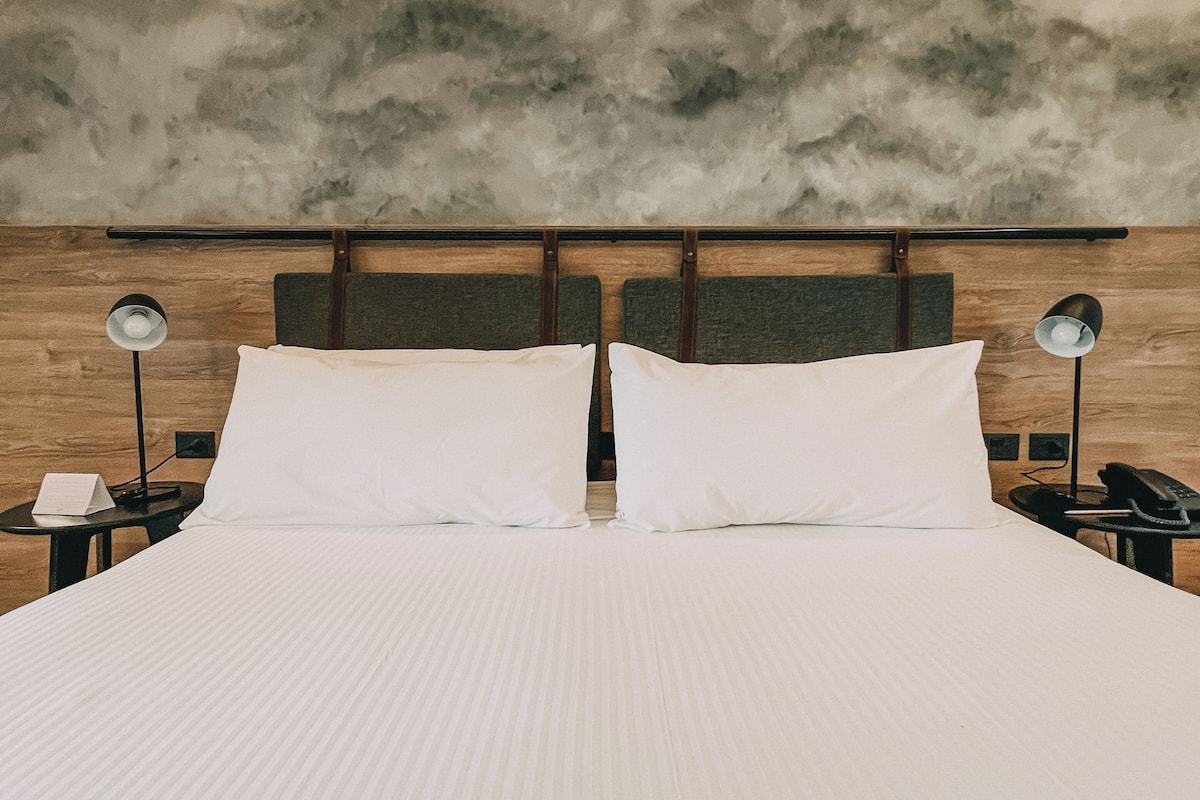 Een hotelkamer met een groot bed, twee nachtkastjes en een gestructureerde wand.