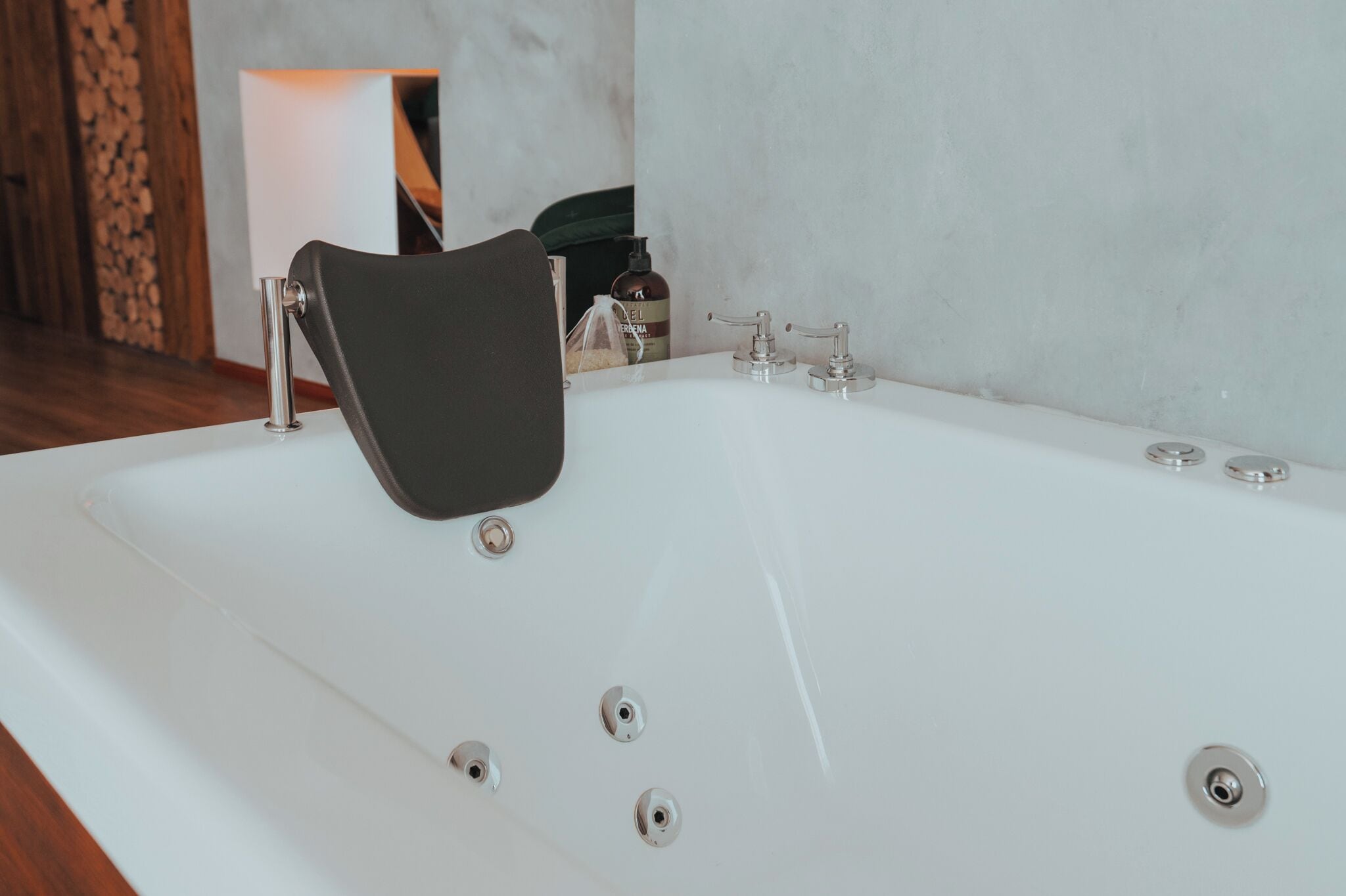 Un baño moderno con una bañera blanca grande, una silla negra y piso de madera.