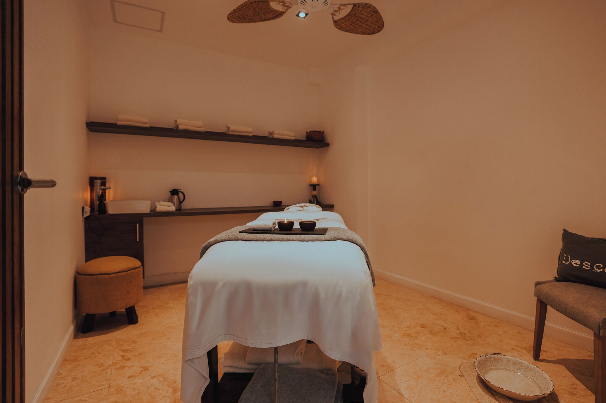 A massage room with a bed, a small table with a tray, a bowl, and a chair.