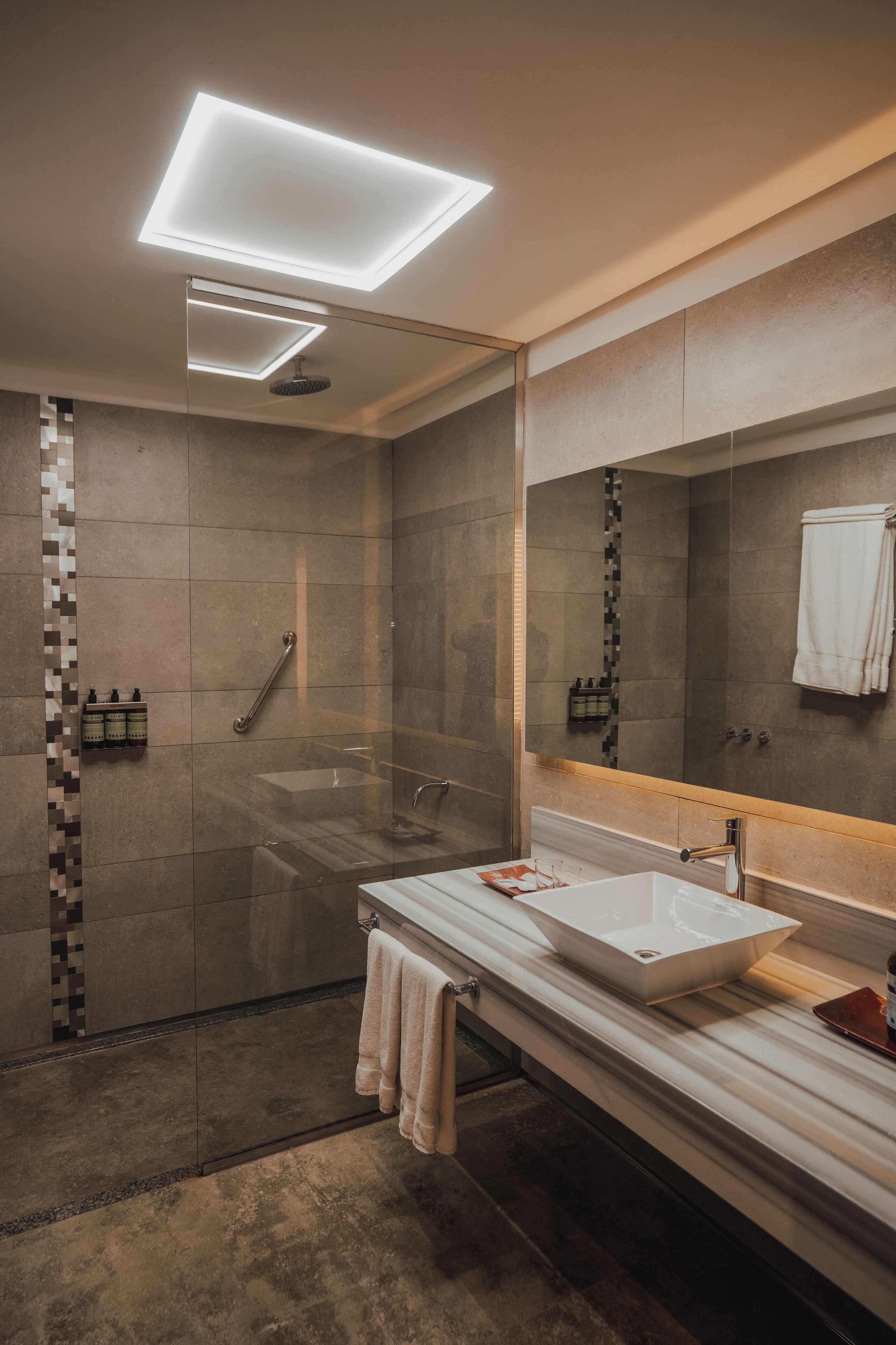 A modern bathroom with a large mirror, a glass-enclosed shower, and a white sink.