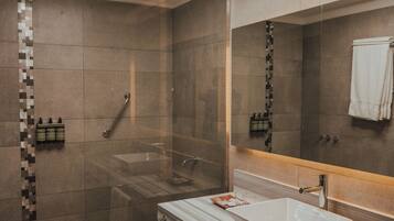 A modern bathroom with a large mirror, a glass-enclosed shower, and a white sink.