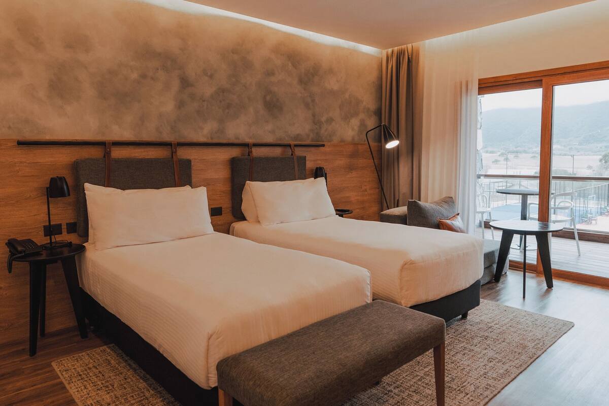 Een hotelkamer met twee bedden, een kleine tafel, een stoel en een balkon met uitzicht.