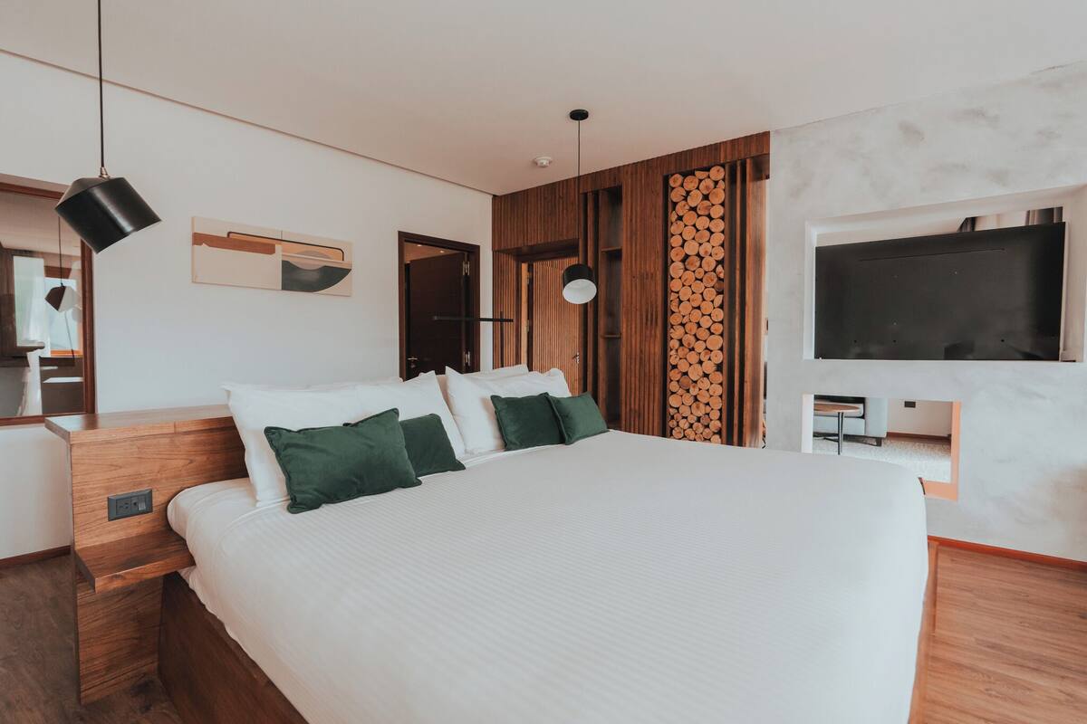 Een moderne slaapkamer met een groot bed, houten hoofdbord, een wandmontage televisie en een houten wandpaneel.