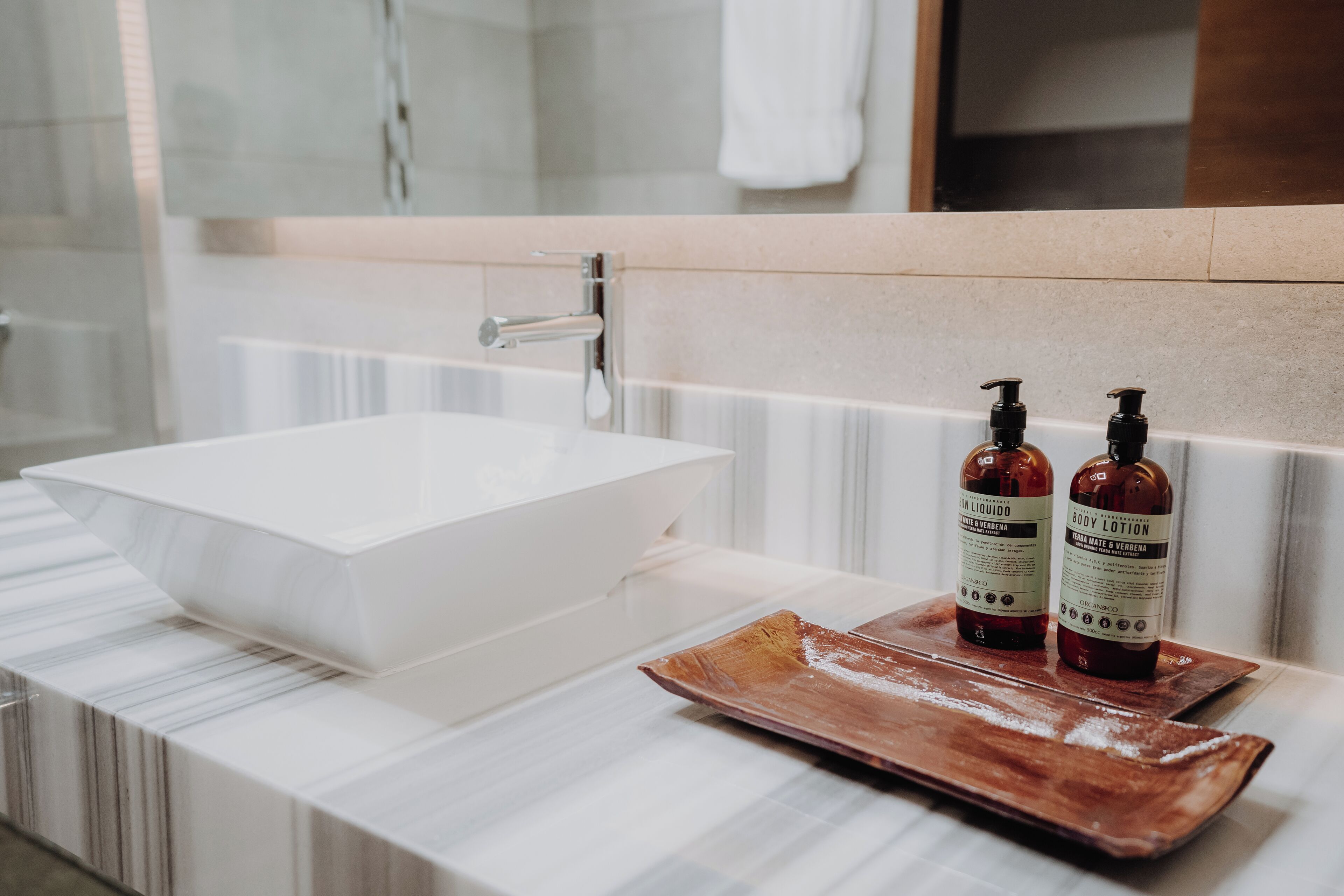 A bathroom with a white marble sink, two bottles of body lotion, and a wooden tray.