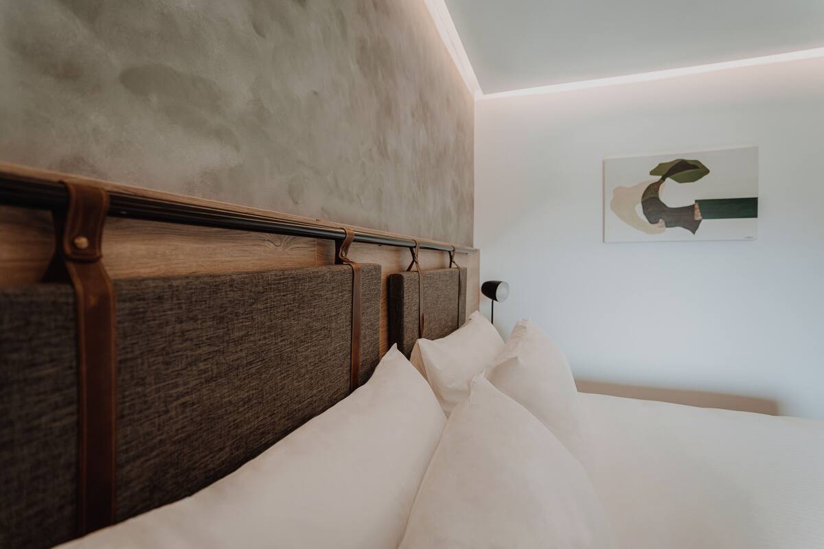Een slaapkamer met een houten hoofdbord, wit beddengoed en een aan de muur bevestigd kunstwerk.