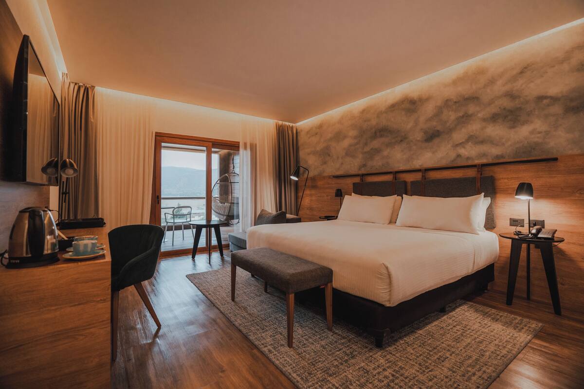 Een hotelkamer met een groot bed, een bureau met stoel, een koffiezetapparaat en uitzicht op de omgeving.