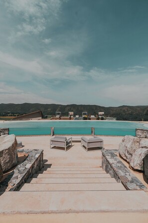 A pool area with steps leading to a lounge area, surrounded by stone walls and overlooking a beach with mountains in the background. - Böden Hotel & Spa, AKEN SOUL (Villa General Belgrano)