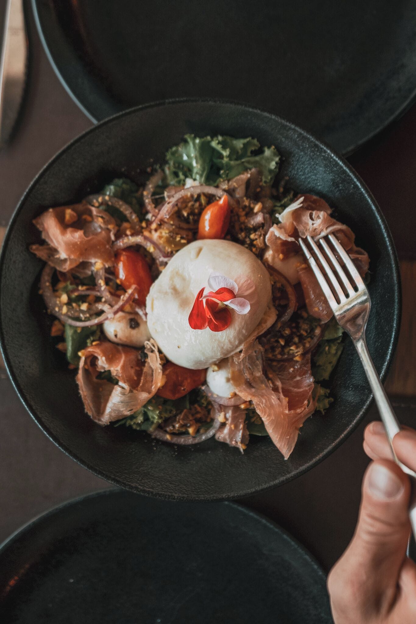 A bowl of food with various ingredients, including a white spherical item and a red flower garnish.