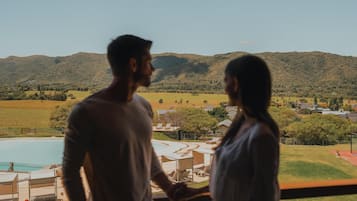 A couple standing by a window overlooking a pool and a mountainous landscape.