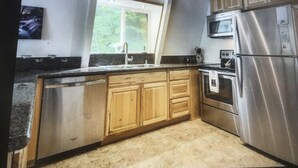 Une cuisine dotée de meubles en bois, d’un réfrigérateur en acier inoxydable, d’un four à micro-ondes et d’une fenêtre donnant sur un paysage verdoyant.