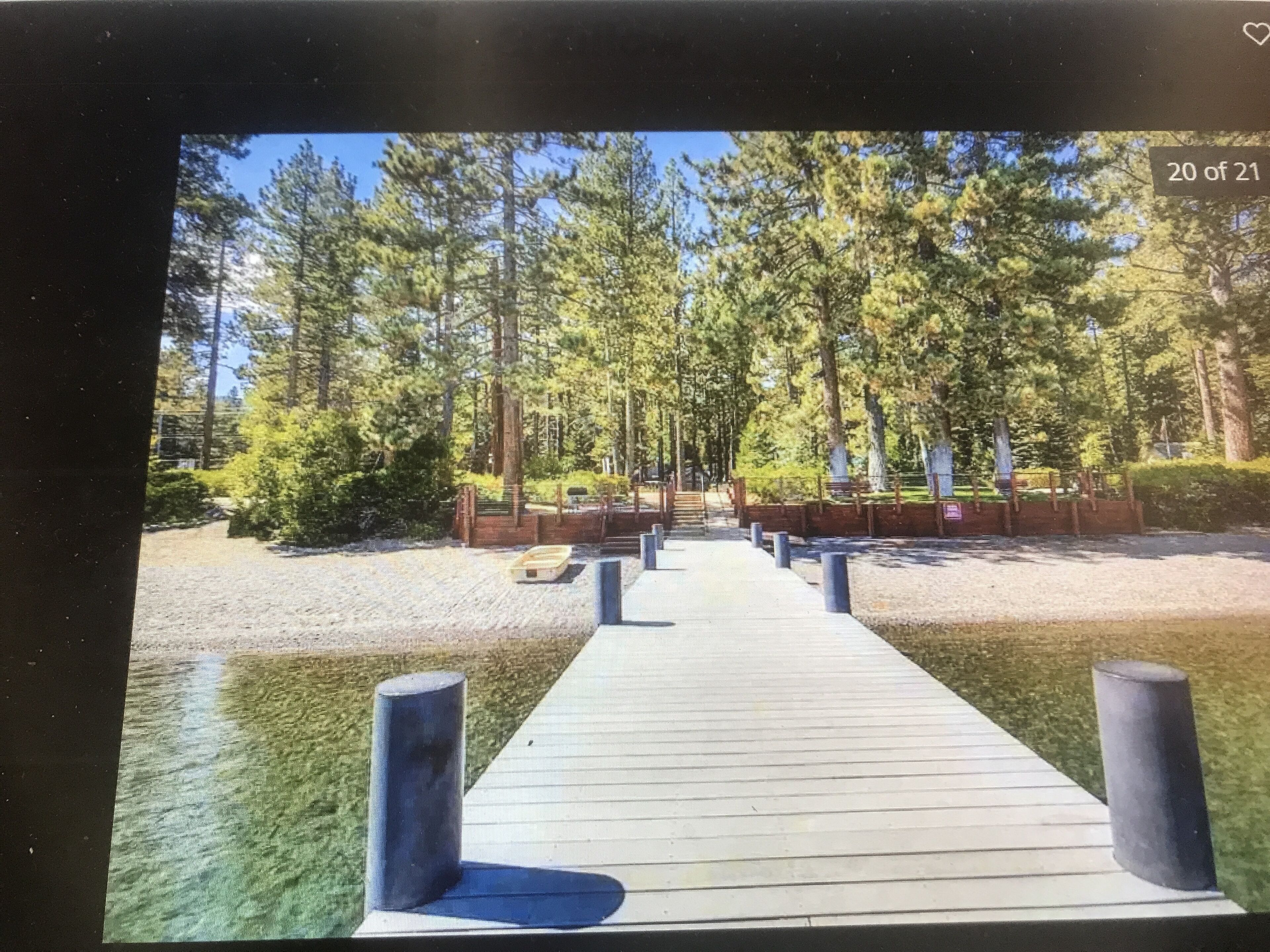 A wooden pathway leading to a dock over a body of water, surrounded by tall trees and greenery.