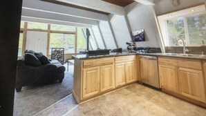 Une cuisine moderne avec des armoires en bois, un grand îlot central et une cuisinière intégrée. Une grande fenêtre offre une lumière naturelle et une vue sur l’extérieur.