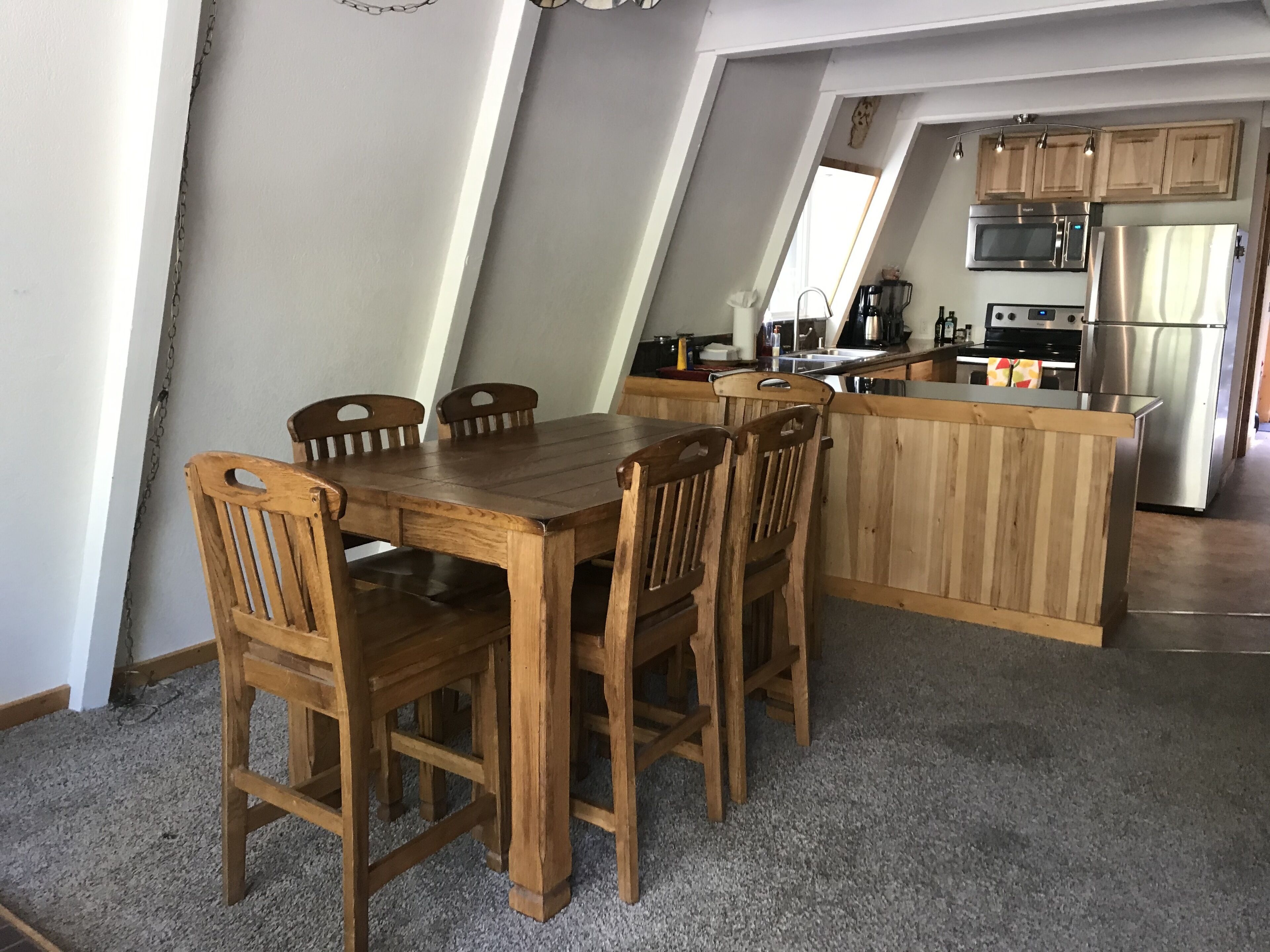 Zona pranzo con tavolo e sedie in legno, cucina con elettrodomestici moderni e soffitto a falde.