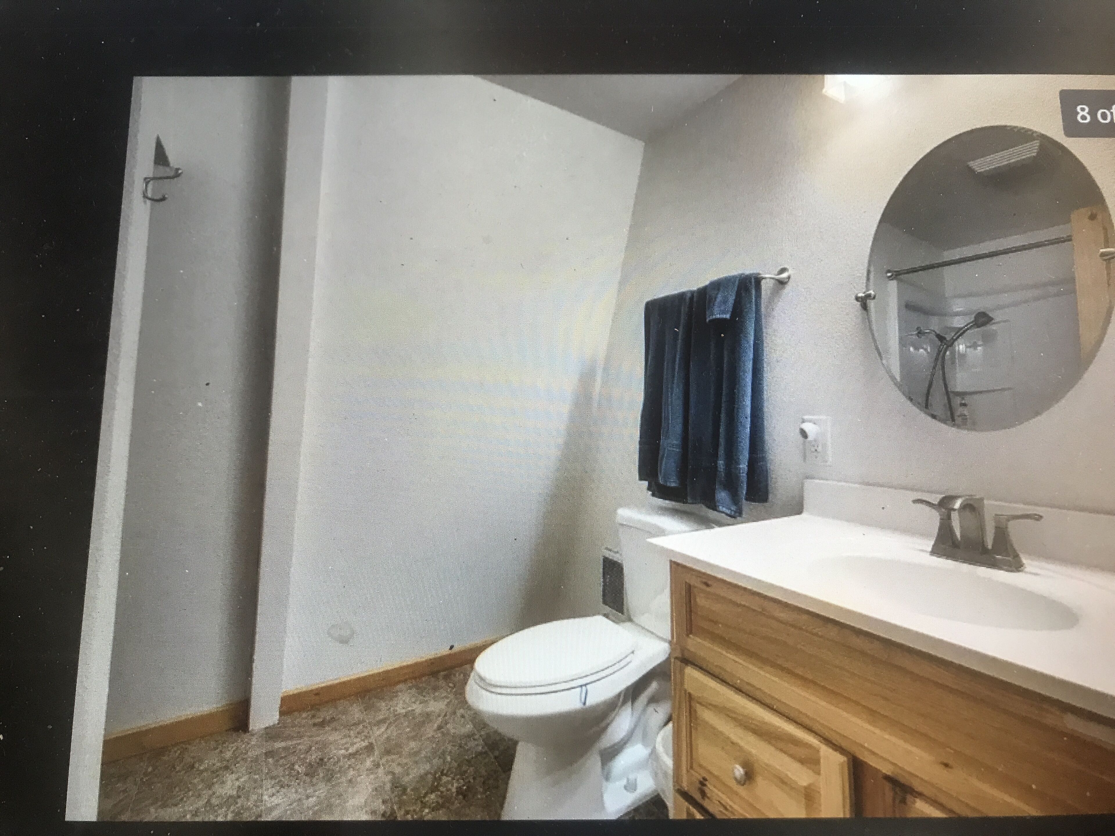 A bathroom with a toilet, sink, wooden cabinet, and a towel hanging on the wall.
