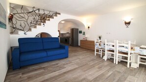 Ein Wohnzimmer mit einem blauen Sofa, einem Essbereich mit einem weißen Tisch und Stühlen sowie einer Küche im Hintergrund.