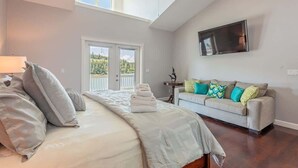 Un dormitorio con cama, sofá, televisor y balcón con vistas.
