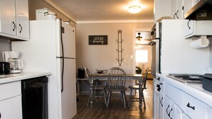 A kitchen with white cabinets, a wooden floor, and a dining area with metal chairs. - Triple H Properties (Eminence)