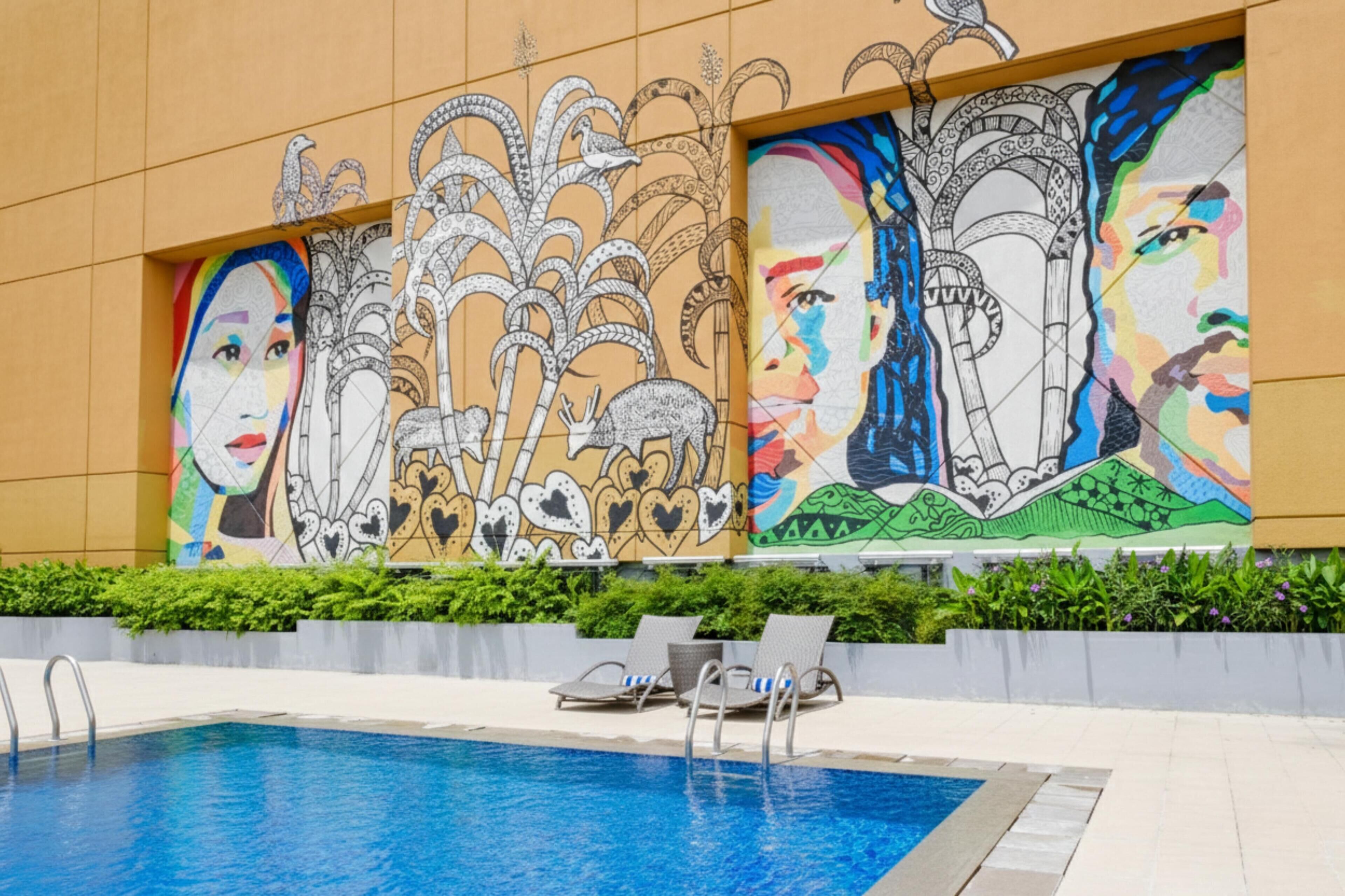 A swimming pool with lounge chairs, a mural with abstract and figurative art, and a building facade with a geometric pattern.