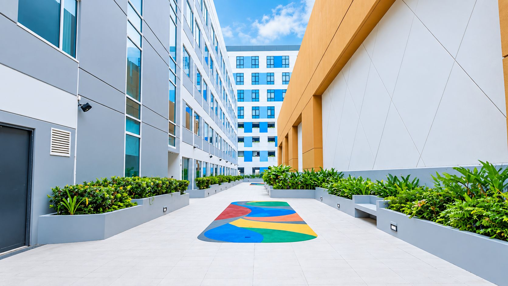 A modern building with a central courtyard featuring a colorful geometric pattern on the floor, surrounded by greenery and white walls.