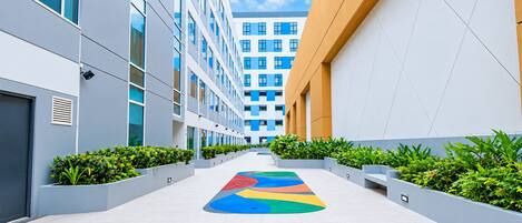 A modern building with a central courtyard featuring a colorful geometric pattern on the floor, surrounded by greenery and white walls.