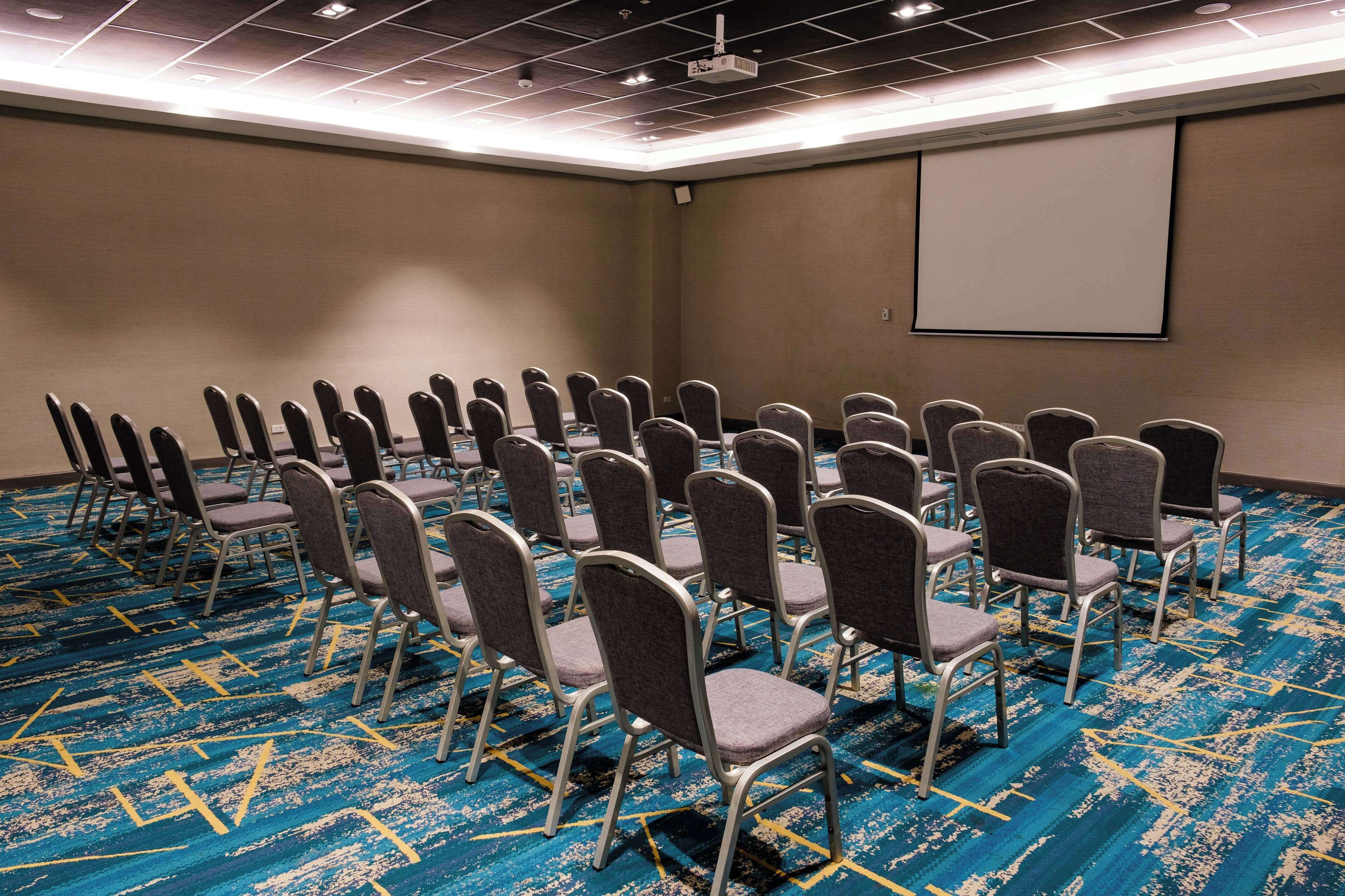 A conference room with rows of chairs, a projector screen, and a carpeted floor.