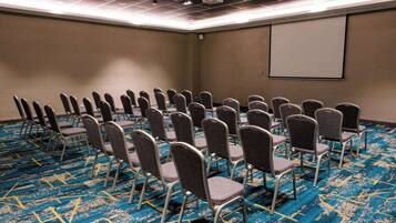 A conference room with rows of chairs, a projector screen, and a carpeted floor.