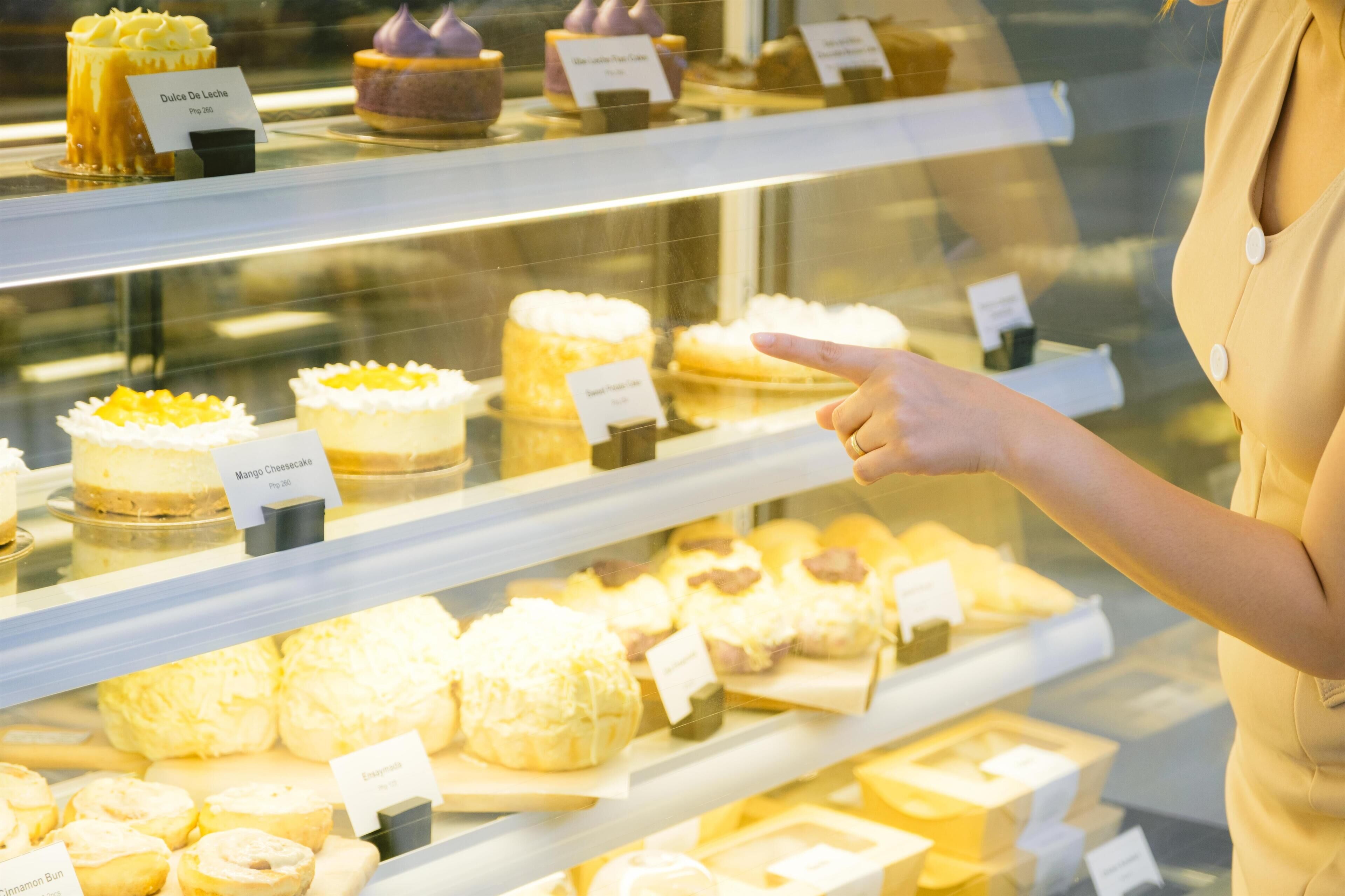 A bakery display case with various pastries and cakes, including a Dulce De Leche and Mango Cheesecake.