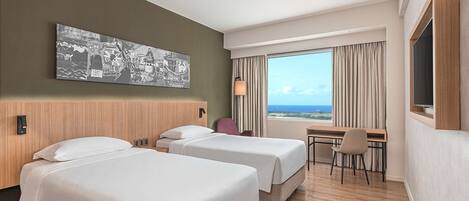 Une chambre d’hôtel avec deux lits, un bureau, une chaise, une grande fenêtre donnant sur un beau paysage et une œuvre d’art accrochée au mur.