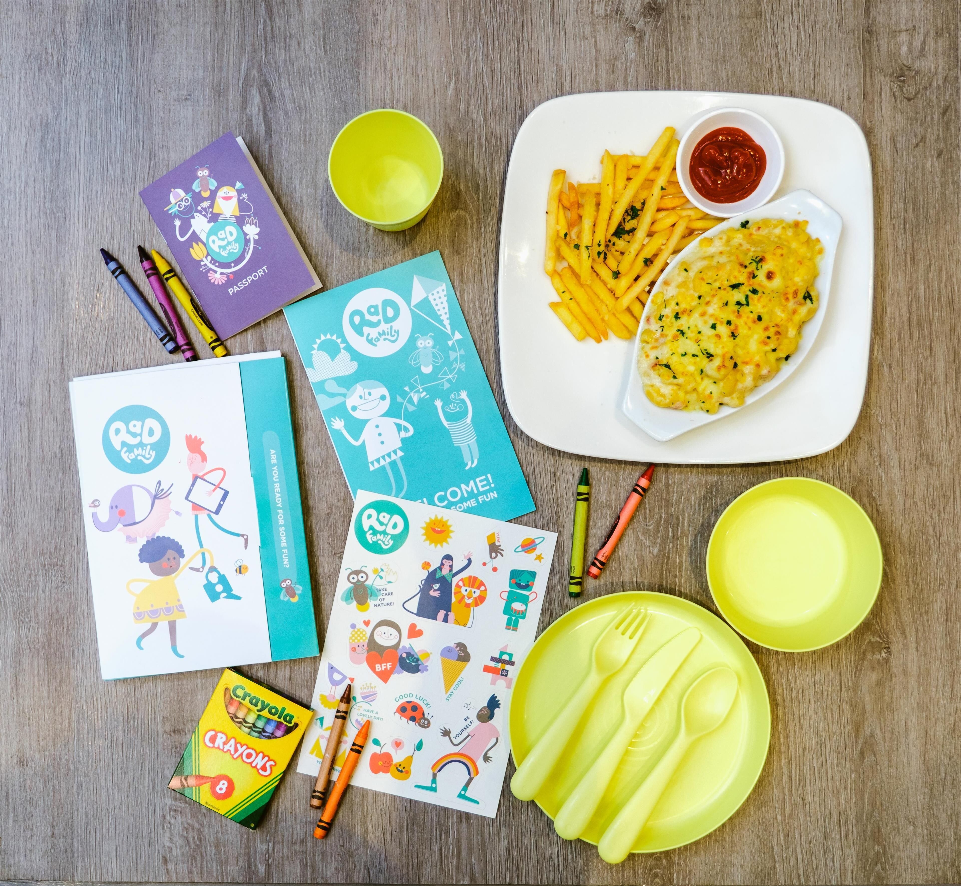 A table with children's activity books, crayons, a plate of food, and cutlery.