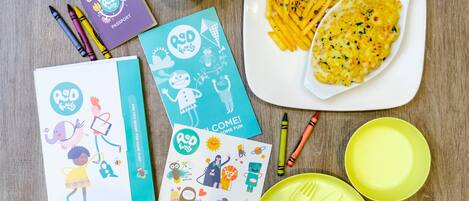 A table with children's activity books, crayons, a plate of food, and cutlery.