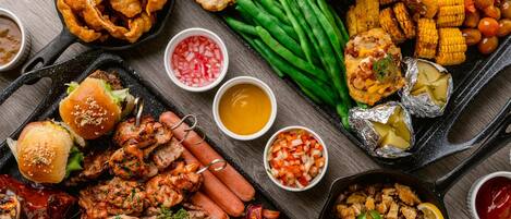 Variedad de alimentos a la parrilla, como salchichas, pollo y verduras, en una bandeja.