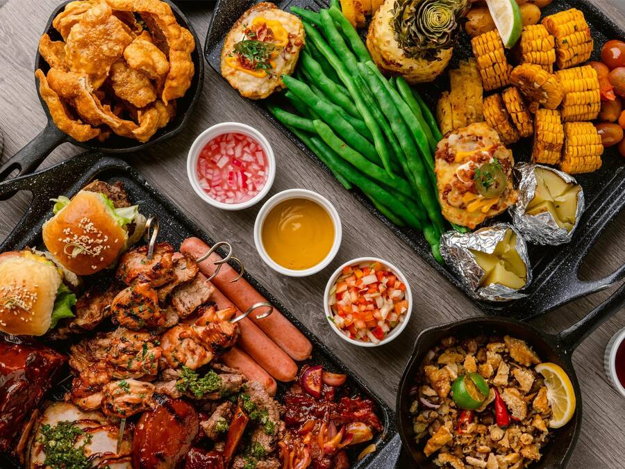 Variedad de alimentos a la parrilla, como salchichas, pollo y verduras, en una bandeja.