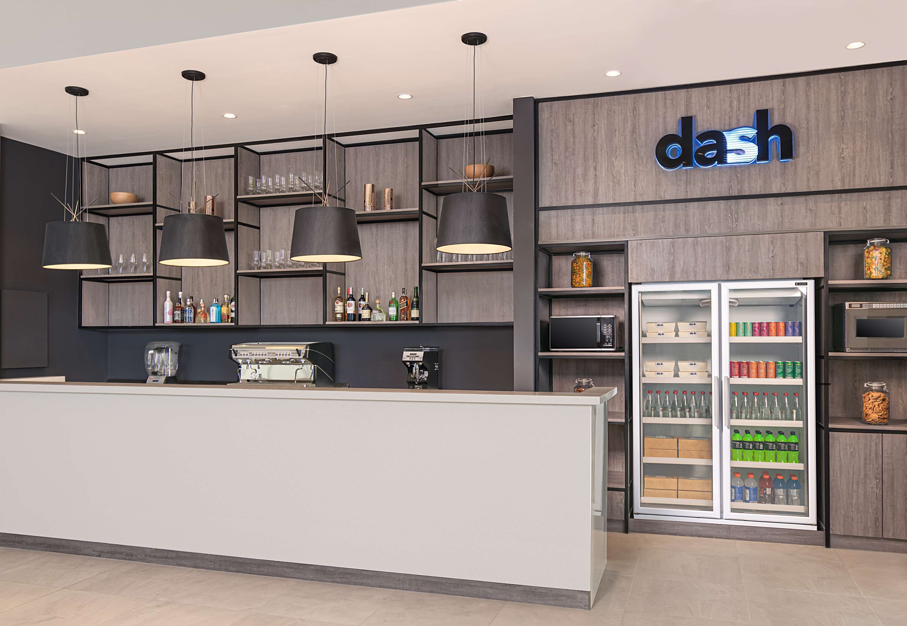 Een moderne bar met een receptiebalie, planken met flessen en een koelkast vol drank.