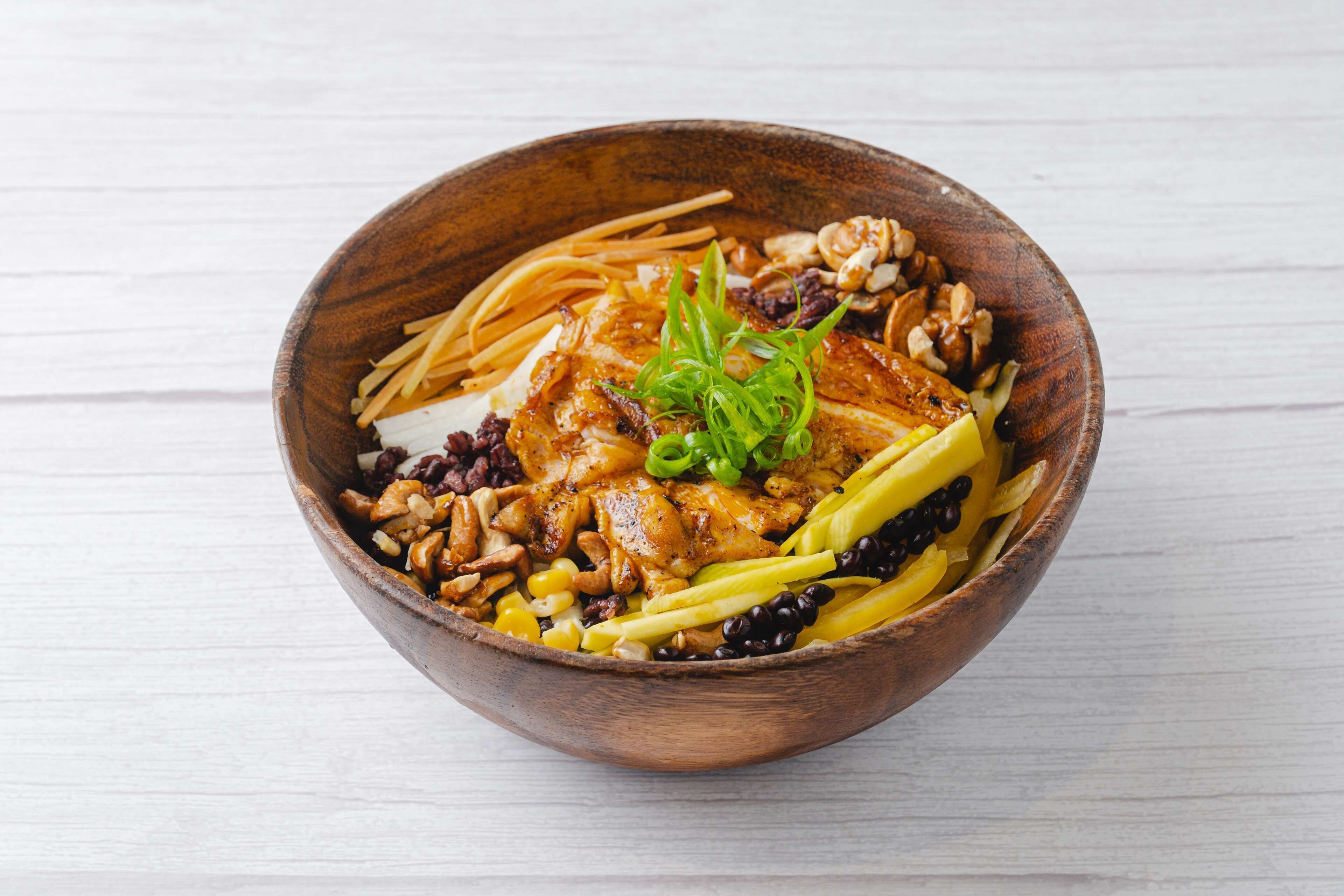 A wooden bowl containing a variety of food items including noodles, meat, and vegetables.