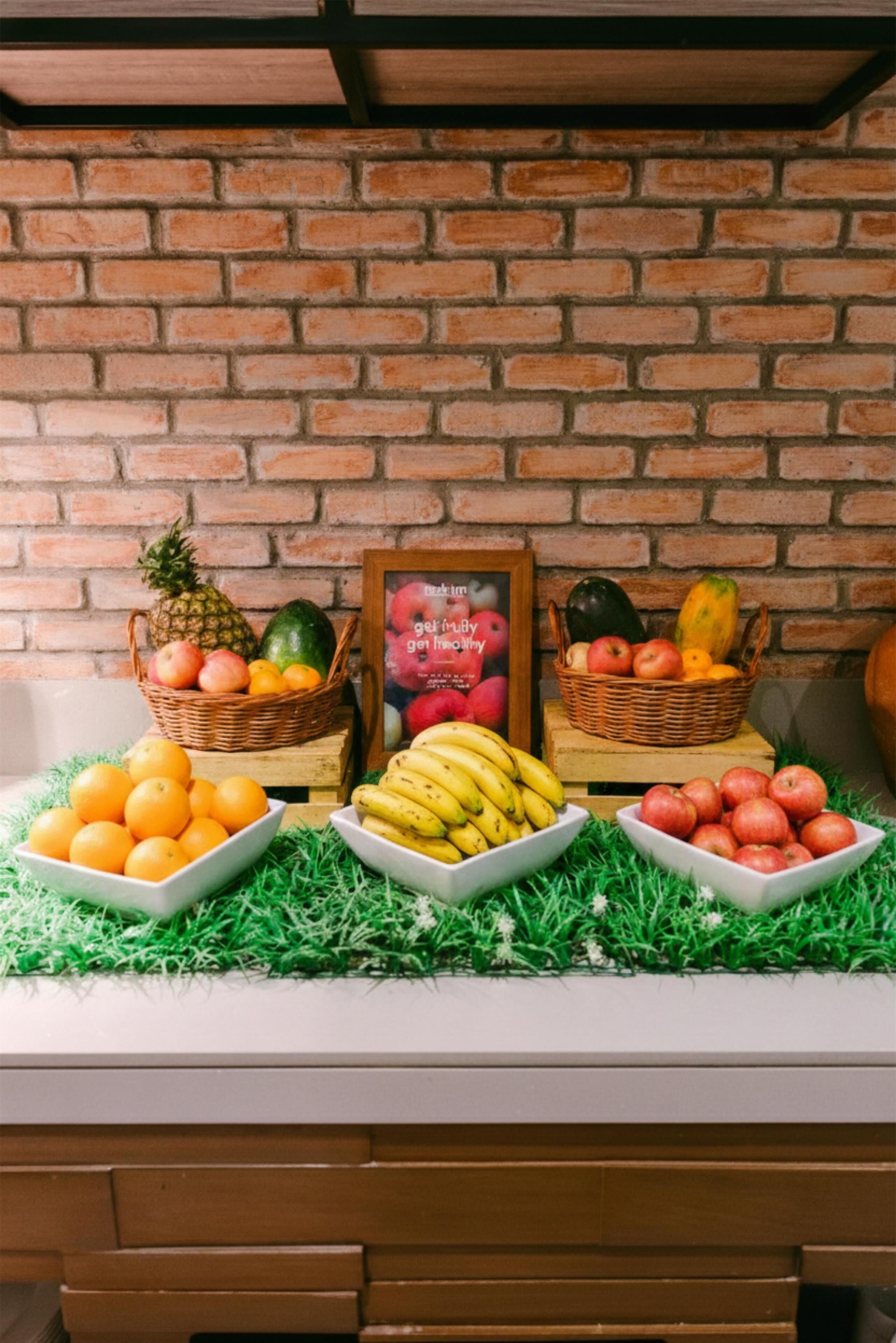 A brick wall, a framed poster, and a table with fruit baskets and bowls.