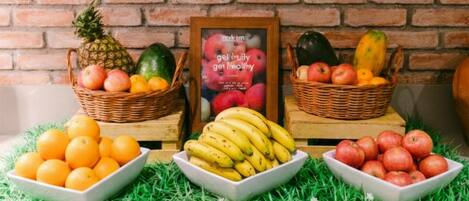 A brick wall, a framed poster, and a table with fruit baskets and bowls.