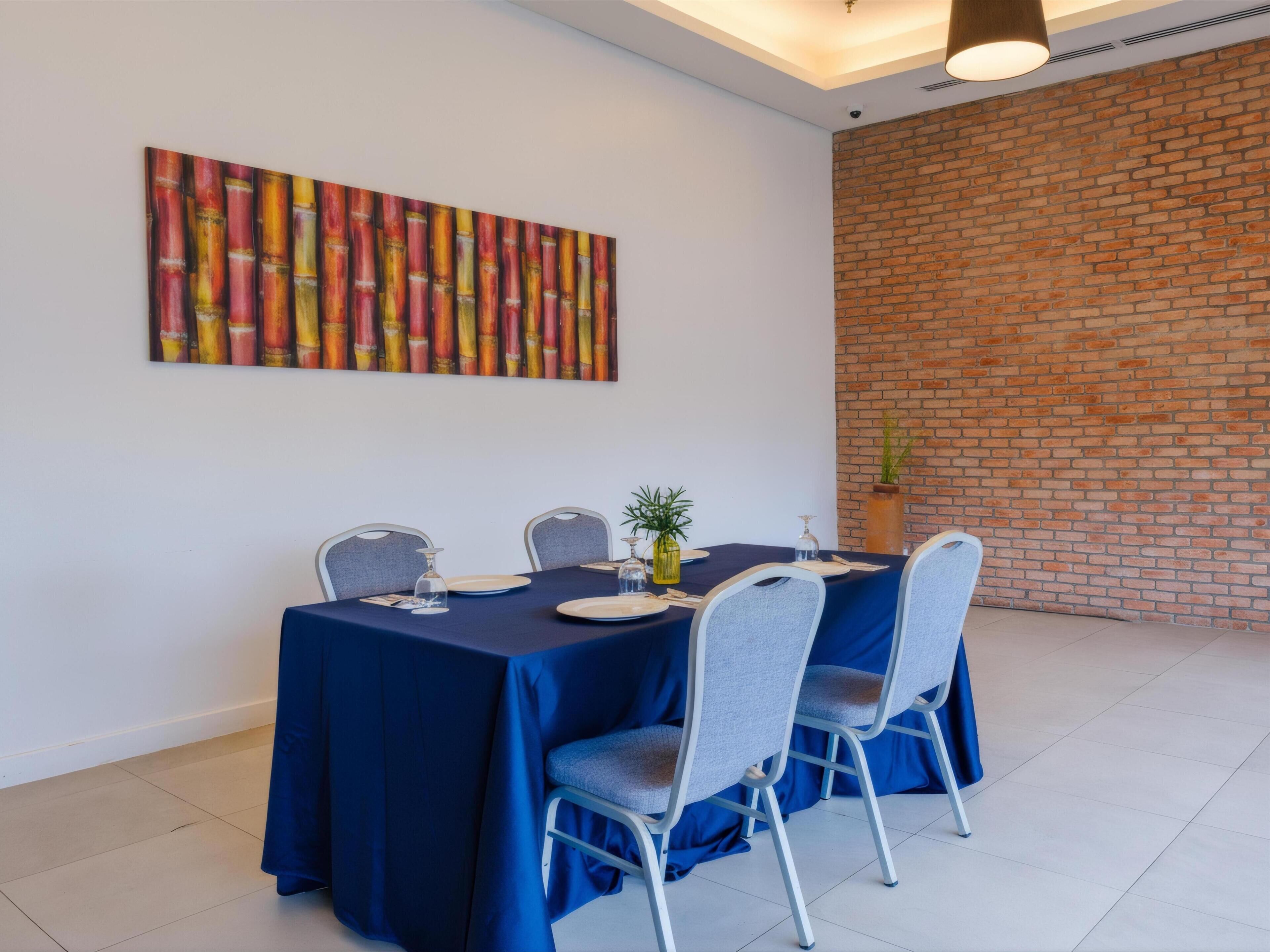 A dining area with a table set for four, chairs, a wall-mounted painting, and a brick wall.