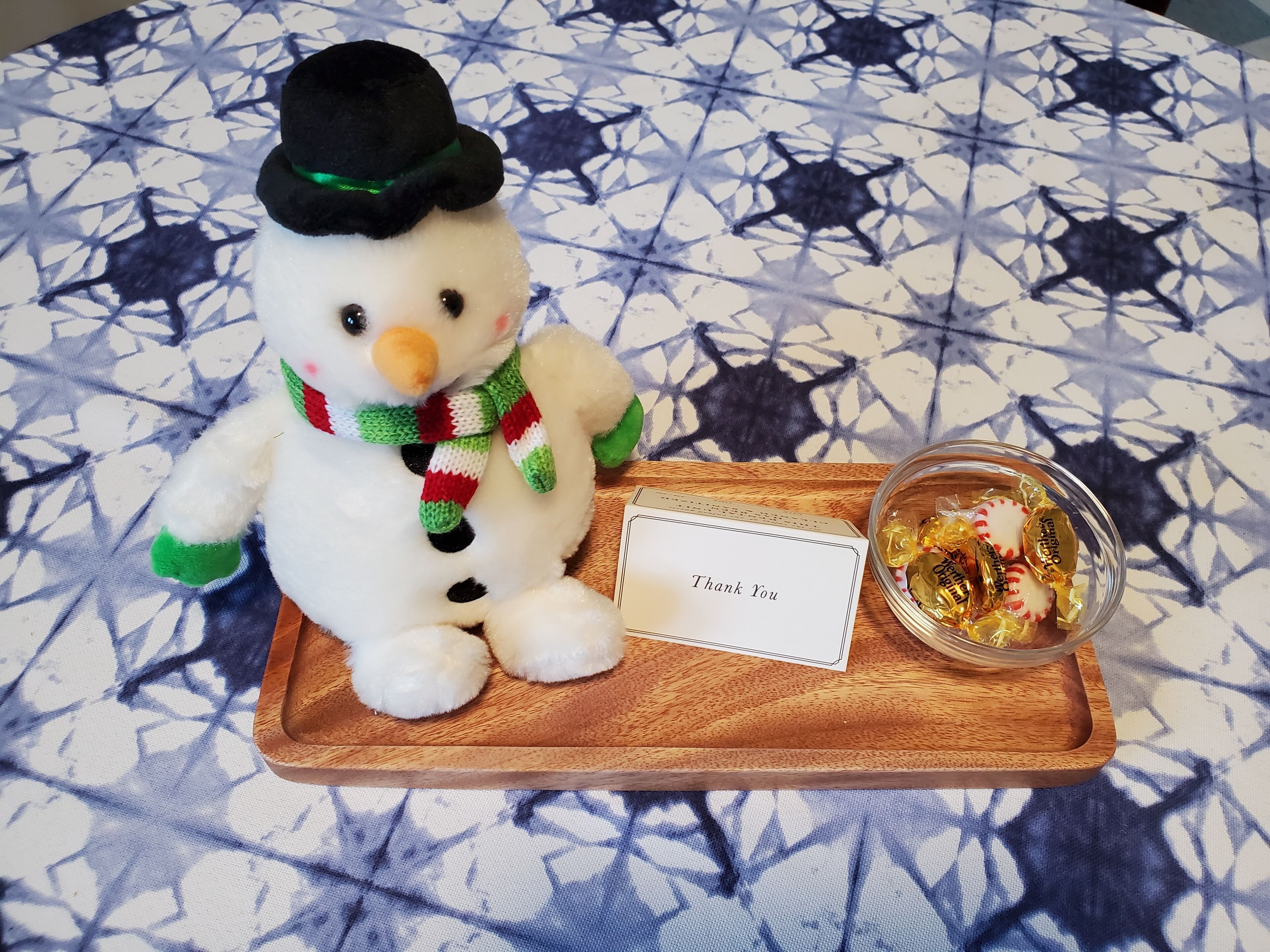 A snowman figurine on a wooden tray with a thank you card and a bowl of candies.