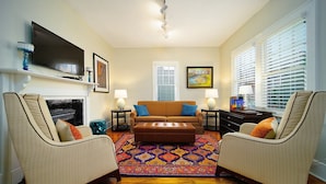 A living room with a sofa, two armchairs, a coffee table, a fireplace, a television, and a patterned rug.