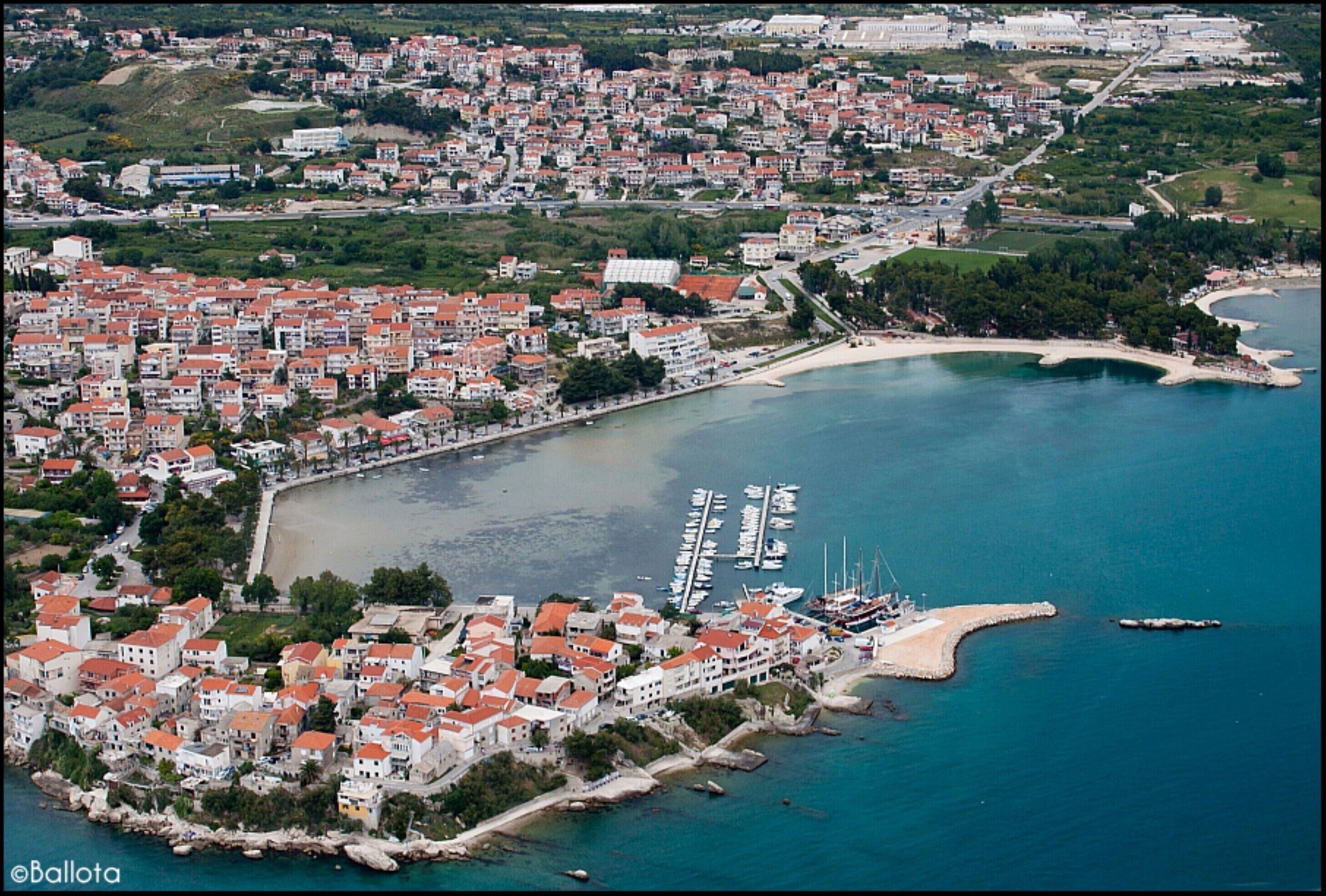 Una vista aerea di una cittadina costiera con edifici fitti, un porto turistico e una spiaggia.