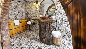 Une salle de bain avec un sol en mosaïque de pierre, une baignoire en bois, un meuble-lavabo en bois avec un vasque et un grand miroir.
