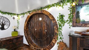 Une pièce rustique avec une grande porte en bois, un meuble en bois et un miroir orné d’un motif représentant un ananas.