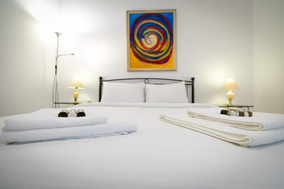 A neatly made bed with white linens, two bedside lamps, and a colorful abstract painting on the wall.