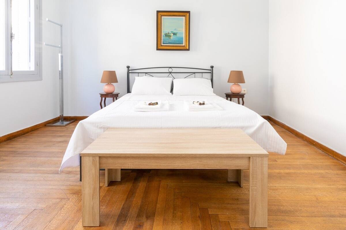 A neatly made bed with white linens, two bedside lamps, a wooden bench, and a framed picture on the wall.
