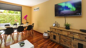 Ein modernes Wohnzimmer mit einem Holzesstisch, schwarzen Stühlen, einem Fernseher an der Wand und einer kleinen Uhr.
