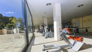 Ein Fitnessstudio mit Trainingsgeräten, darunter Laufbänder und Fahrräder, und einem großen Fenster mit Blick auf eine gepflegte Grünfläche.