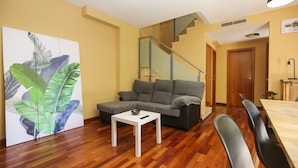 Ein Wohnzimmer mit grauem Sofa, einem kleinen weißen Tisch und einem Holzesstisch mit Stühlen.