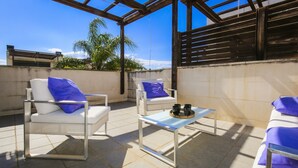 Eine Terrasse im Freien mit zwei weißen Stühlen, einem kleinen Tisch und einem blauen Kissen.