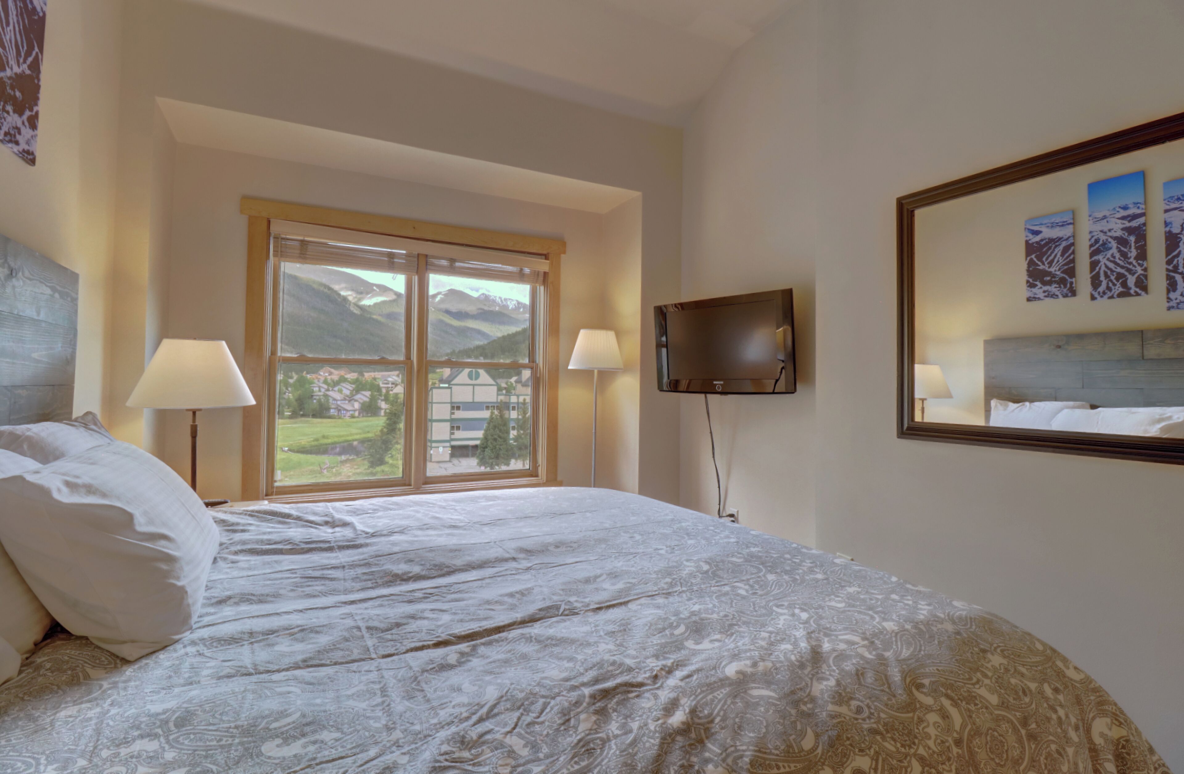 Une chambre d’hôtel avec un grand lit, deux lampes de chevet, un téléviseur fixé au mur et une fenêtre donnant sur la montagne.