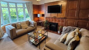 A living room with two sofas, a glass coffee table, a fireplace, and a TV mounted on a wooden wall. - Robin Hill (St Austell)